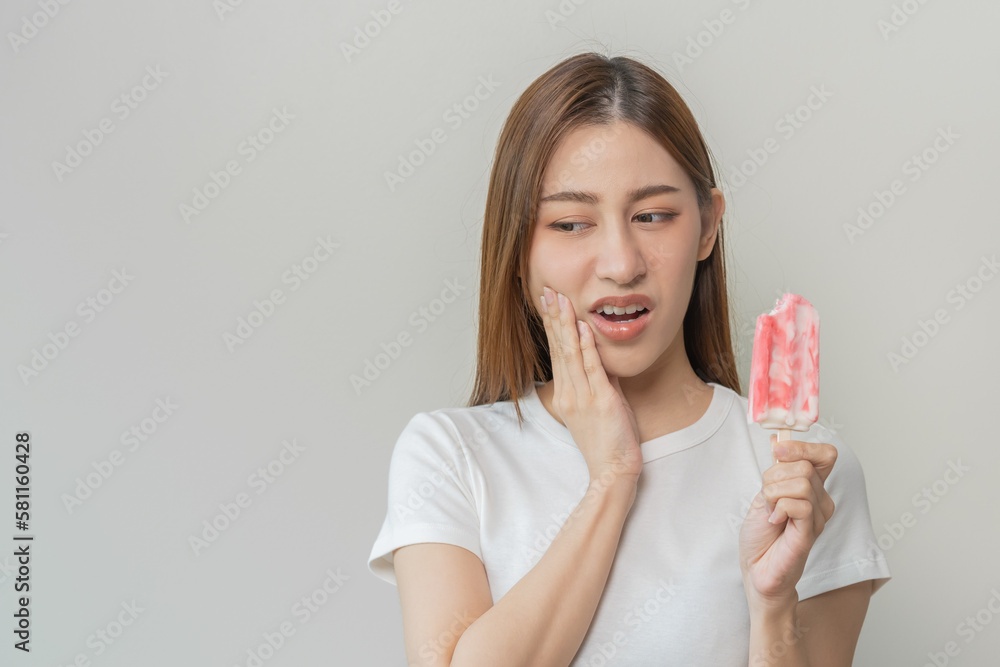 Face expression suffering from sensitive teeth and cold, asian young woman, girl hand touching her cheek, feeling hurt, pain eating ice cream, lolly. Toothache molar tooth at home, dental problem. Face expression suffering from sensitive teeth and cold, asian young woman, girl hand touching her cheek, feeling hurt, pain eating ice cream, lolly. Toothache molar tooth at home, dental problem.