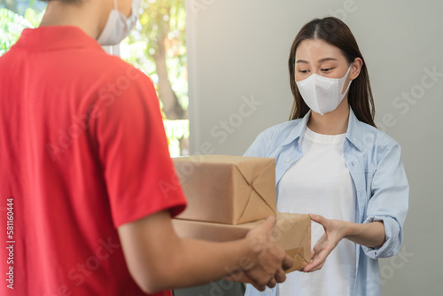 Asian young woman  client received a delivery of cardboard box  parcel from delivery  postman  wearing face mask due to lockdown  quarantine of covid-19 at the door  entrance of her home  house.