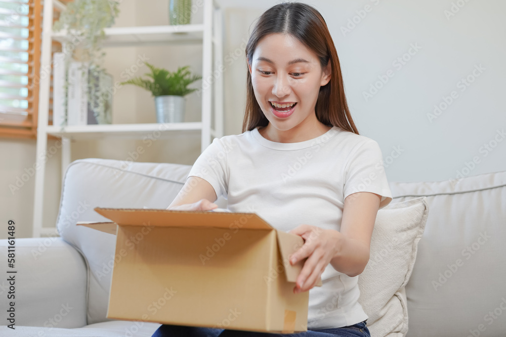 Happy excited, asian young woman, girl customer sitting on sofa at home, opening and unpacking cardboard box carton parcel after buying ordering present, shopping online, delivery service concept. Happy excited, asian young woman, girl customer sitting on sofa at home, opening and unpacking cardboard box carton parcel after buying ordering present, shopping online, delivery service concept.