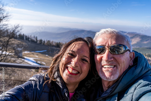 middle aged couple wearing winter clothes taking a selfie over a mountain