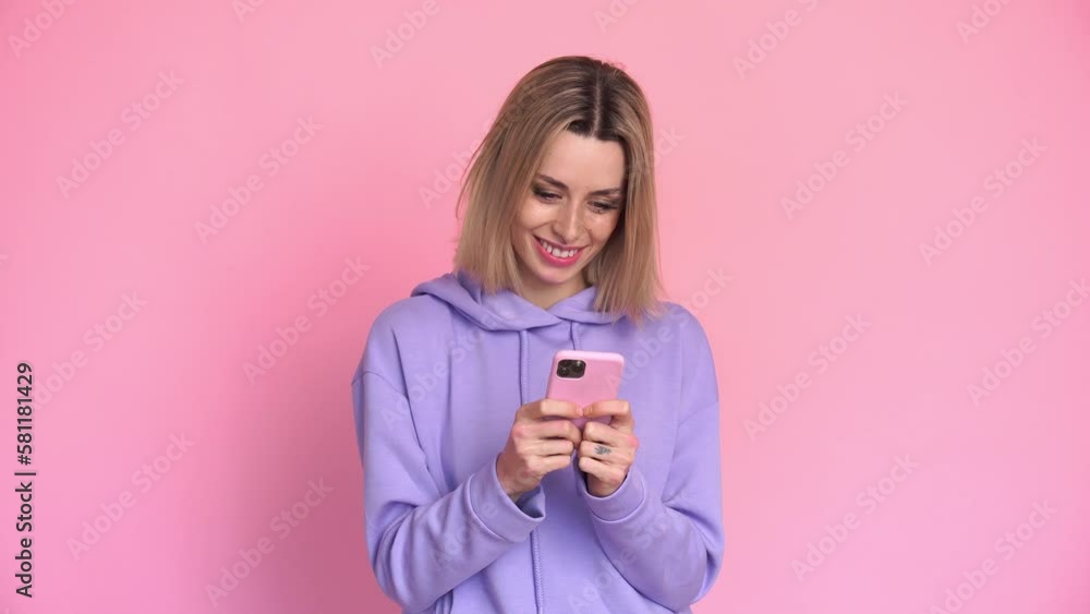 Cheerful woman using smartphone on pink background in studio