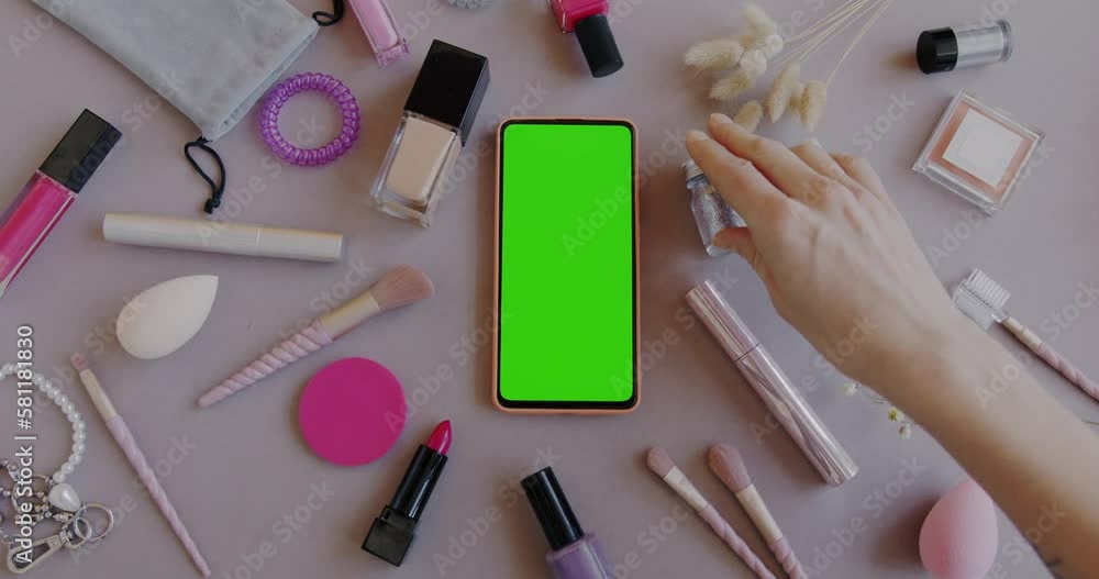 Top view of green screen chroma key mobile phone and female hand using make-up accessories on gray background. Modern technology and cosmetics concept. Top view of green screen chroma key mobile phone and female hand using make-up accessories on gray background. Modern technology and cosmetics concept.