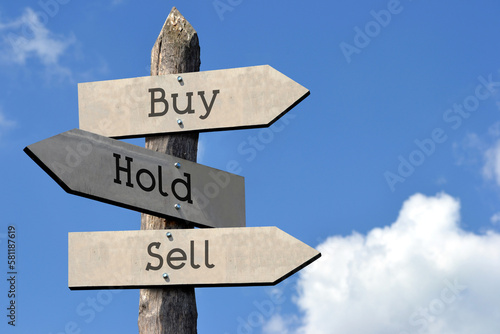 Buy  hold  sell - wooden signpost with three arrows  sky with clouds