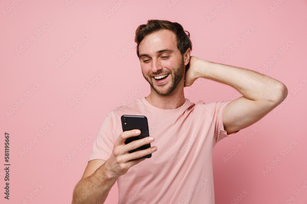 Cheerful man using mobile phone and touching his head isolated over pink wall Cheerful man using mobile phone and touching his head isolated over pink wall