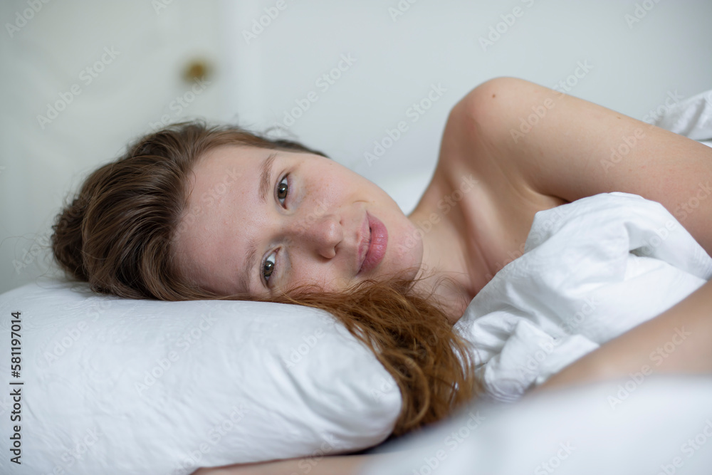 Young happy beautiful sleepy woman in the bed in bedroom at home in the morning lying under white blanket, enjoy resting, sleep well, wake up and smile. Good morning Young happy beautiful sleepy woman in the bed in bedroom at home in the morning lying under white blanket, enjoy resting, sleep well, wake up and smile. Good morning
