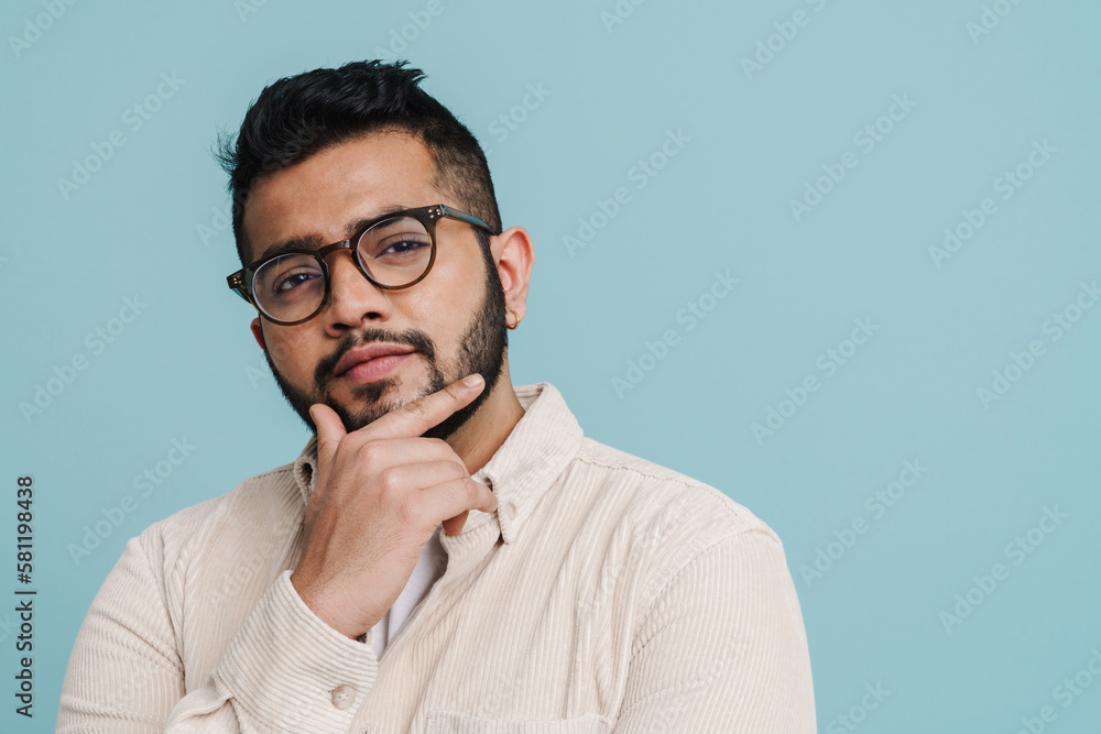 Thoughtful indian guy touching his chin isolated over blue wall Thoughtful indian guy touching his chin isolated over blue wall