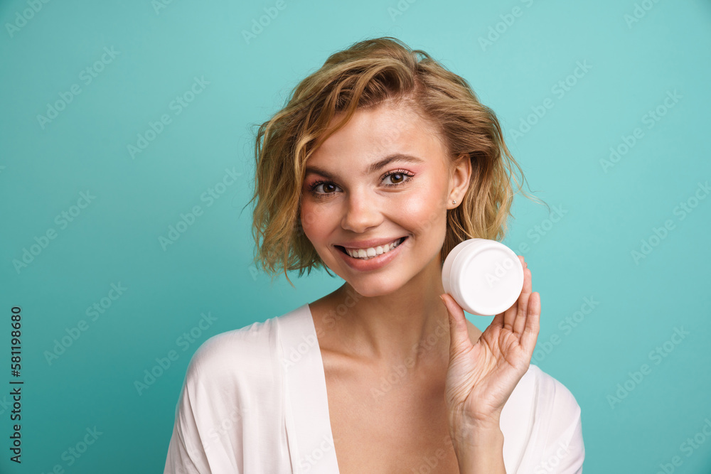 Woman holding facial cream jar and smiling at camera isolated over blue wall Woman holding facial cream jar and smiling at camera isolated over blue wall