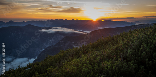 View of an early sunrise during summer as seen from the viewpoint 5 fingers on the Krippenstein mountain toward the valley with fog coming over the mountains and mountain ranges in the background.