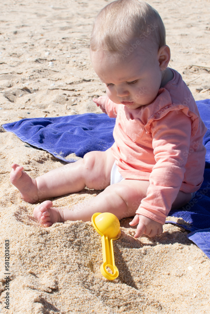 Baby girl playing in the sand with plastic toy. 8 months old baby with blonde hair at the beach. Baby girl playing in the sand with plastic toy. 8 months old baby with blonde hair at the beach.