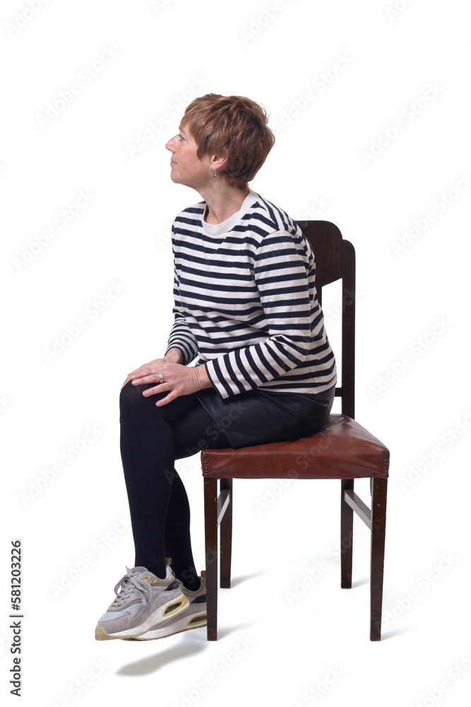 side view full length portrait of a woman in skirt, striped sweater and sneakers sitting on chair and legs crossed looking away on white background side view full length portrait of a woman in skirt, striped sweater and sneakers sitting on chair and legs crossed looking away on white background