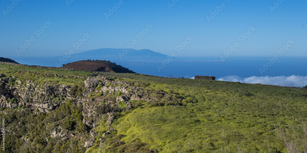 Verdes prados con la silueta de la isla de La Palma al fondo.