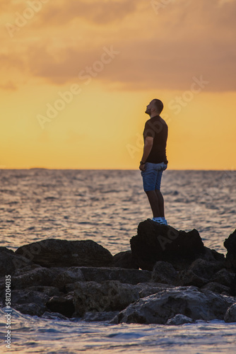 man standing on a rock in the sea watching the sunset