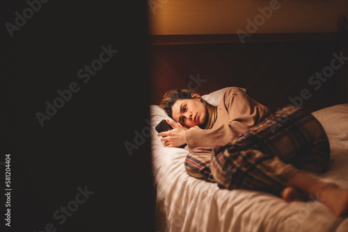 Fotografie Young depressed woman using mobile phone crying on bed at night feeling sad and depressed victim of cyber bullying or broken heart suffering depression in desperate woman expression