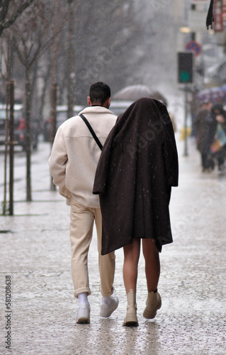 Two people walking on the sidewalk in the city street on a rainy day without an umbrella, couple, winter, cold