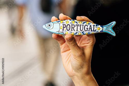 Hand of a young woman holding a sardine-shaped magnet on the street. Souvenir concept from Lisbon, Portugal.