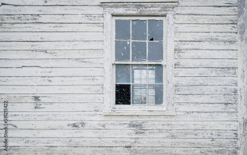 Old house exterior with old wooden boards and broken window. White painted wood siding with antique finish. Snow falling 