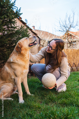 A young girl student is petting and feeding and playing with her pet dog labrador in backyard 