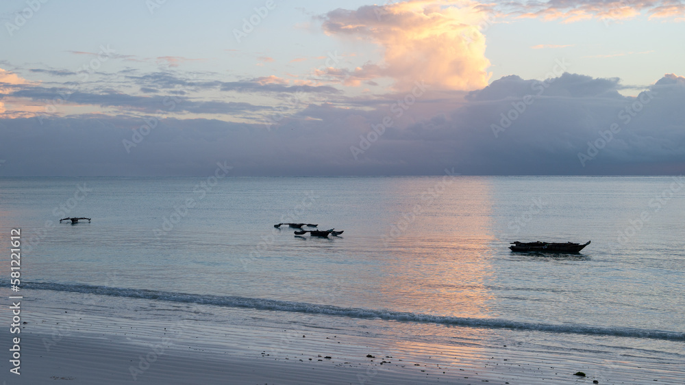 Naklejka premium Sunrise in the Indian Ocean of Zanzibar (Tanzania) with its traditional wooden fishing boats (ngalawa) and the native fishermen