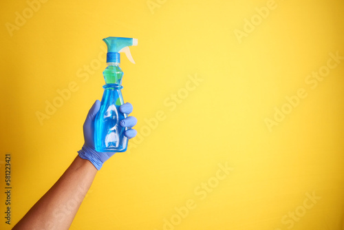 holding a plastic cleaning bottle against yellow background 