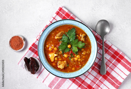 Moroccan Harira Soup in blue bowl at grey concrete table top. Harira is Moroccan Cuisine dish with lamb or beef meat, chickpeas, lentils, tomatoes, ciliantro. Ramadan Iftar Food. Copy space. Top view photo