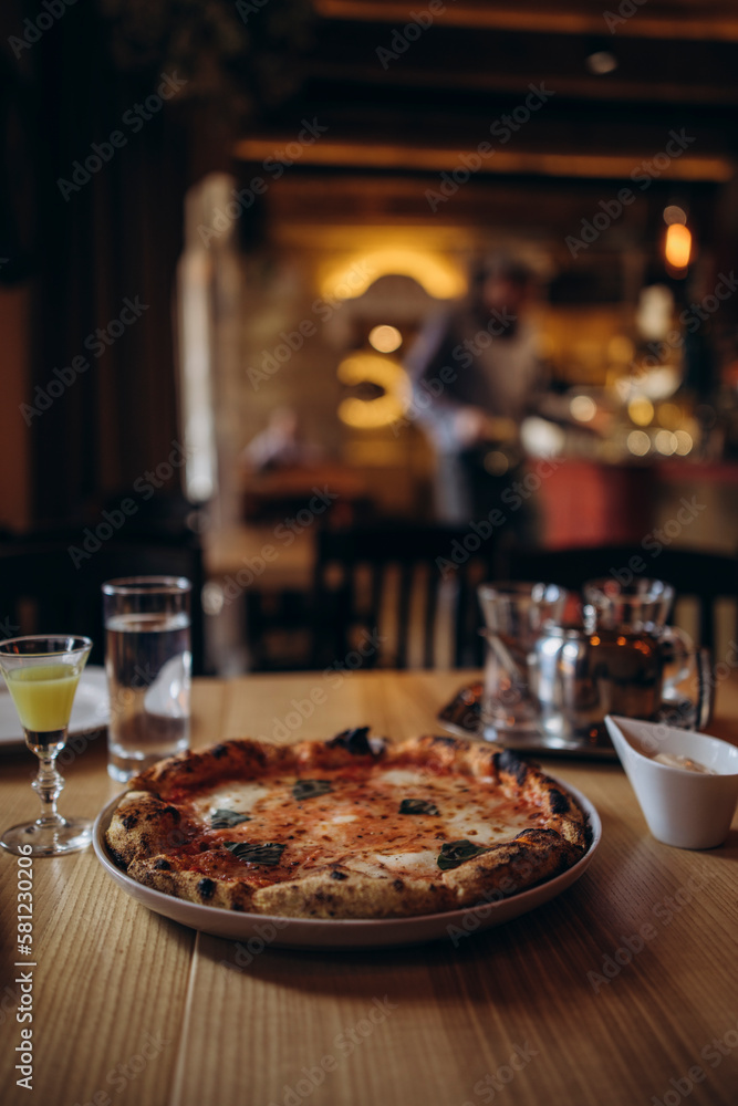 pizza margherita on a plate in a cafe with limoncello and a glass of water. neapolitan pizza margherita with burnt edges. wood fired pizza pizza margherita on a plate in a cafe with limoncello and a glass of water. neapolitan pizza margherita with burnt edges. wood fired pizza