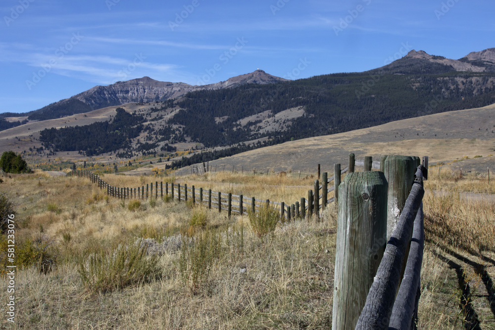American West landscape of farm land fence line, blue sky, and Rocky Mountains