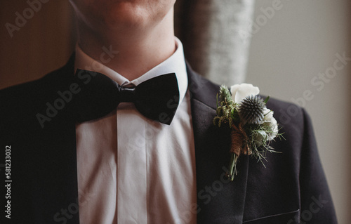 Close up of grooms shoulder wearing tux with buttonhole of thistle and rose
