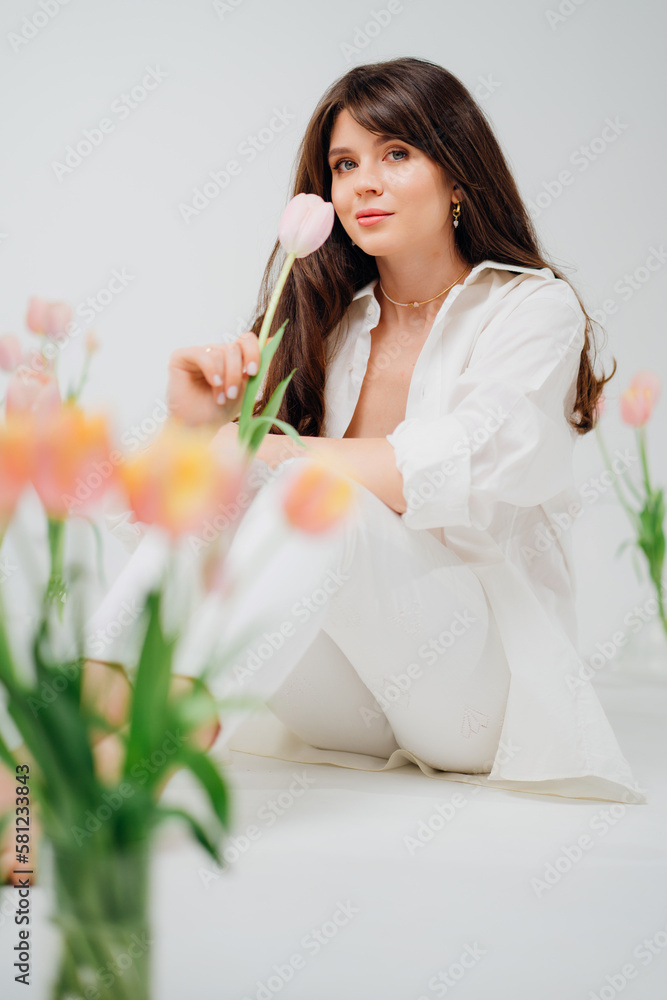gentle brunette in white sits on the floor with vases of tulips