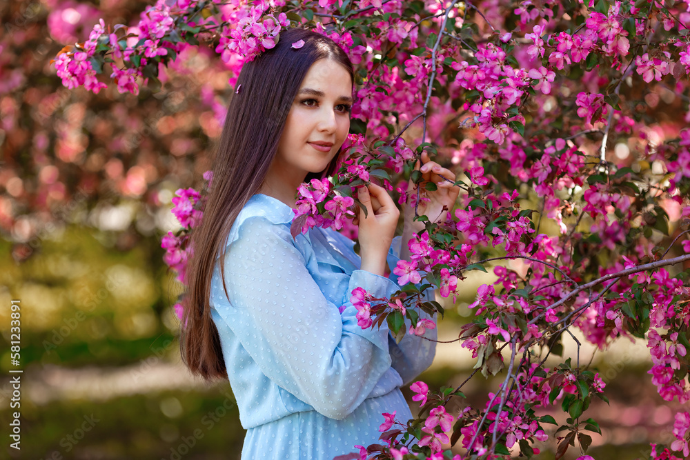 A girl , ong hair ,blue dress, stands near a pink blooming apple tree A girl , ong hair ,blue dress, stands near a pink blooming apple tree