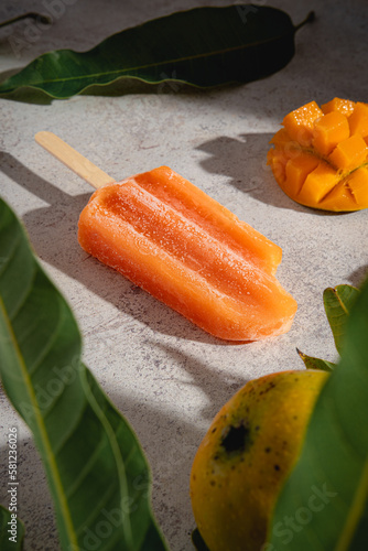 primer plano de paleta de helado de mango en un fondo rustico con espacio para copy y hojas de mango y fruta tropical