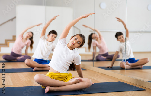 Girl doing exercises in lotus pose with her family in gym.