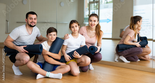 Cheerful mother and father with teen daughter and son posing with gymnastic mats before exercising at yoga class