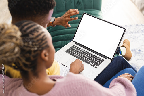 Happy african american couple sitting on sofa and using laptop with copy space in living room