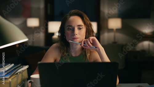 Pensive woman watching screen at dark apartments closeup. Girl tie hair pencil