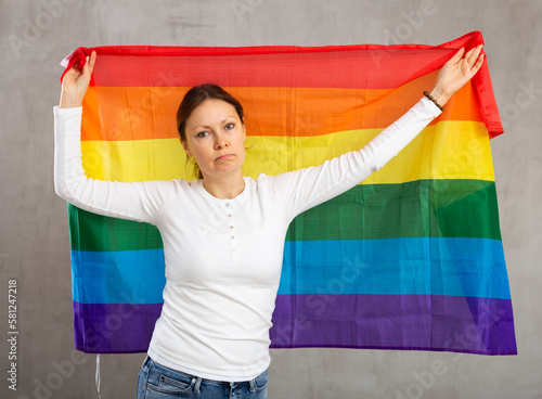 Upset adult woman holding big LGBT flag in her hands