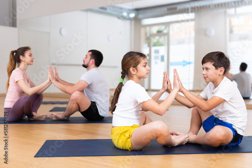 Kids and their parents doing pair yoga exercises in gym during family training.