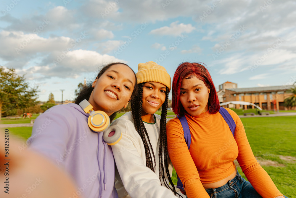 multiracial group of three teenage girl friends using a smart phone to take photos together. classmates and friendship. youth culture and technology