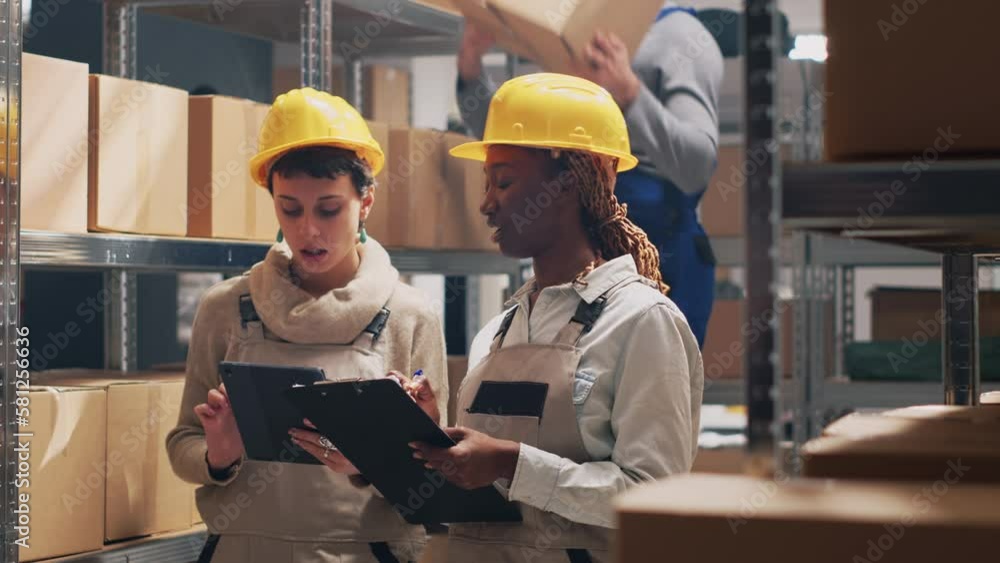 Multiethnic team of supervisors counting boxes of goods placed on warehouse racks, looking at merchandise products in packages. Young women in overalls working in storage room. Multiethnic team of supervisors counting boxes of goods placed on warehouse racks, looking at merchandise products in packages. Young women in overalls working in storage room.