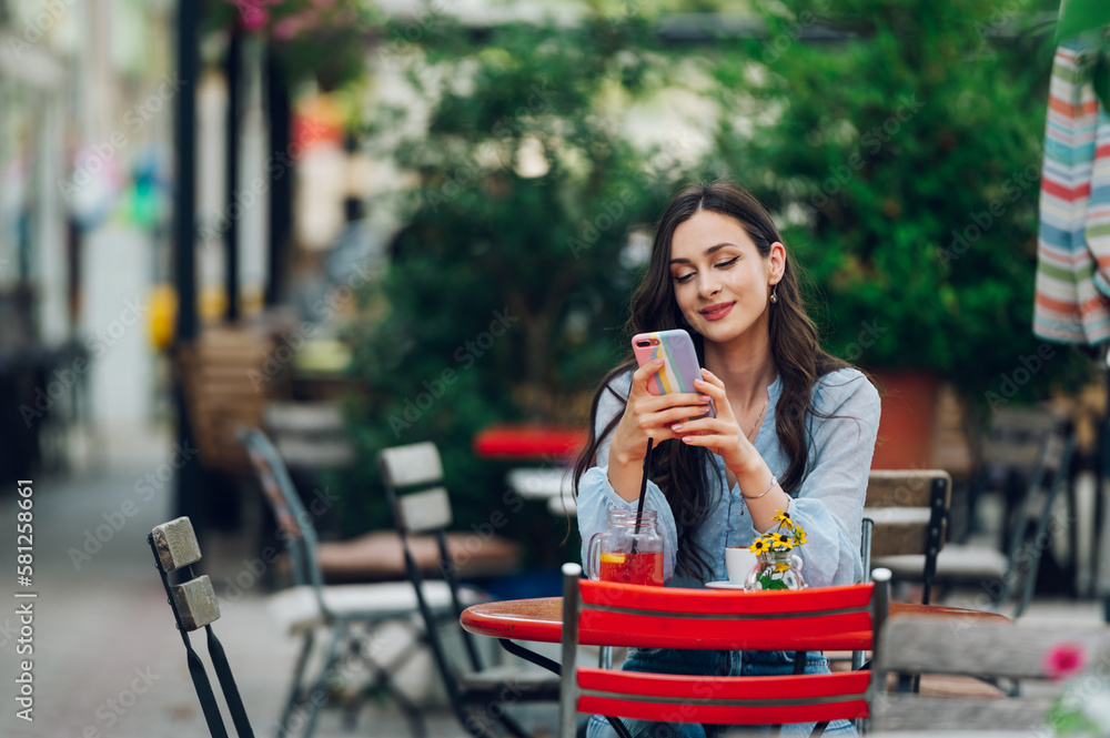 Portrait of a beautiful woman sitting in a street cafe and using a smartphone