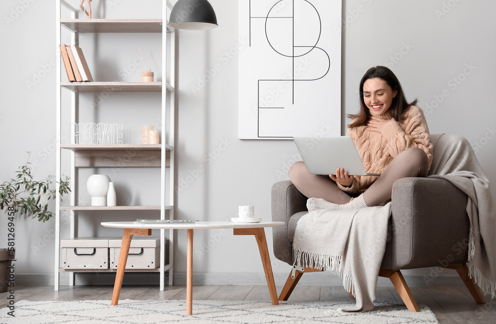 Young woman using laptop in soft armchair at home - obrazy, fototapety, plakaty 