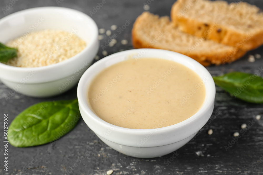 Bowls with tasty tahini, sesame seeds and spinach on dark wooden background, closeup Bowls with tasty tahini, sesame seeds and spinach on dark wooden background, closeup