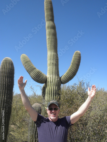 Smiling man in hat and purple t-shirt raises arms to mimic saguaro cactus
