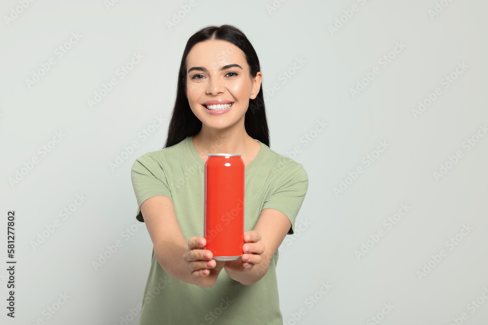 Beautiful happy woman holding red beverage can on light grey background Beautiful happy woman holding red beverage can on light grey background