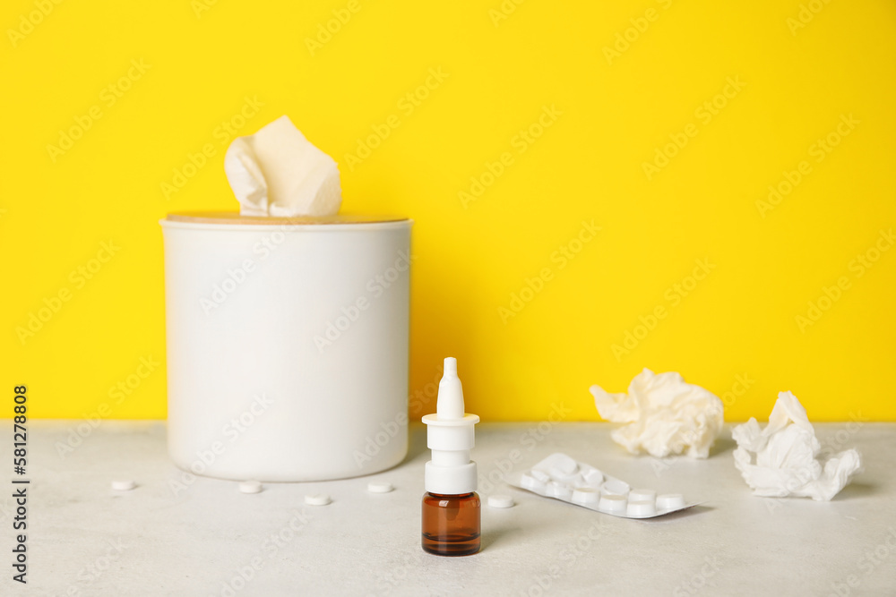Nasal drops with pills and tissue box on table near yellow wall. Allergy concept Nasal drops with pills and tissue box on table near yellow wall. Allergy concept