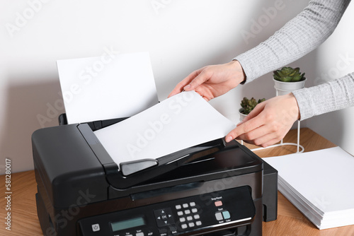 Woman loading paper into printer at wooden table indoors, closeup