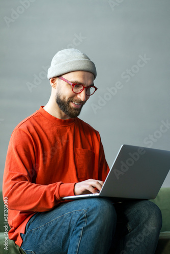 Portrait smiling successful man, programmer using laptop typing on keyboard working freelance project sitting at workplace. Modern bearded hipster watching training courses, planning startup in office