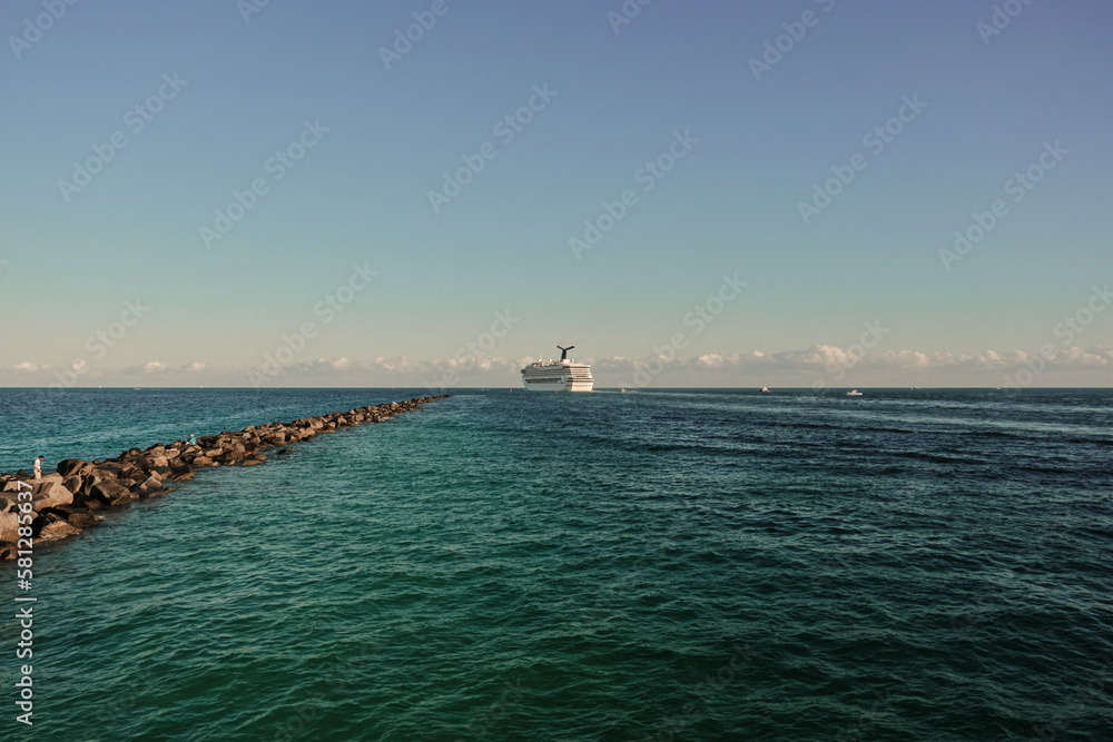 huge tourist cruise ship setting sales while moving away in South Pointe Beach in a clear sky and beautiful blue sea, Miami, Florida, United States