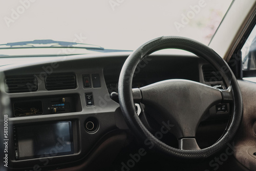 Black classic car interior. Steering wheel, speedometer, display and multimedia dashboard. Detail of car interior inside. Manual gear stick.