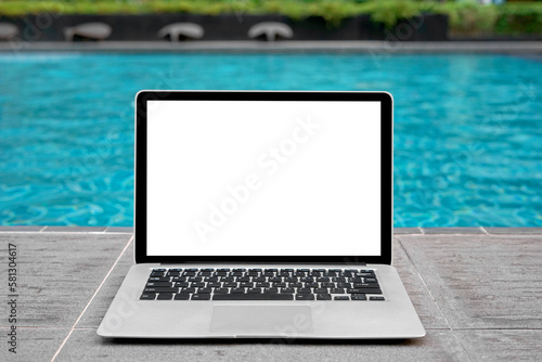 Laptop with blank screen for creative design on floor near swimming pool edge background. Computer notebook with monitor clipping path for present landing page design. Laptop computer mock up template