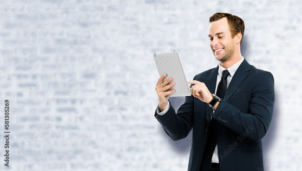 Portrait of smiling businessman in black suit using touchpad tablet pc, white bricks wall background. Success in business concept studio picture. Copy space for ad text. Portrait of smiling businessman in black suit using touchpad tablet pc, white bricks wall background. Success in business concept studio picture. Copy space for ad text.